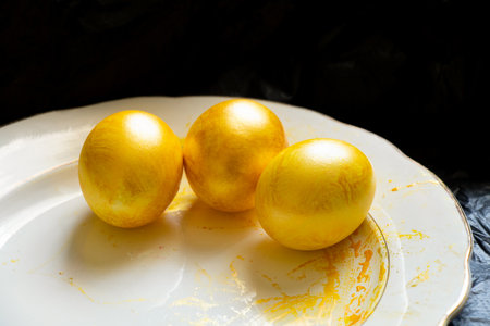 Three eggs painted yellow lie on a white plate on a black background, Easter eggsの写真素材