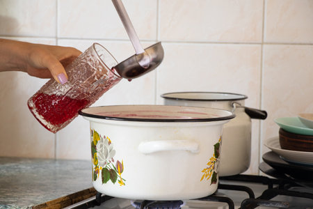 A girl pours freshly brewed homemade fruit compote into a glass in the kitchen, tasting the fruit...