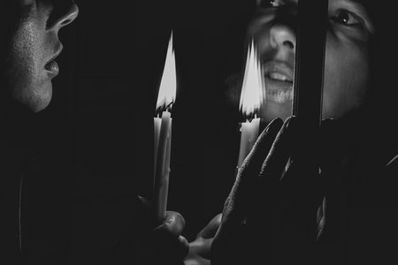 Girl with a candle in the dark near the mirror, looking in the mirror with a candle, black and white...