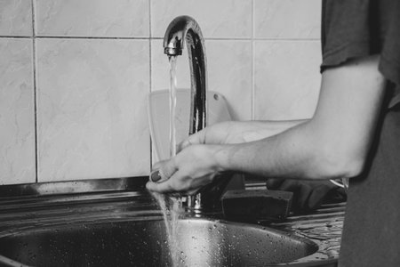 Person washes their hands under the tap in the kitchen in an apartment, black and white photoの写真素材