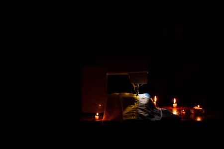 The Ukrainian flag is sewn on a sewing machine on a table with candles in the dark of a house