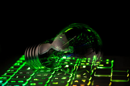 Incandescent light bulb lies on the backlit laptop keyboard at night in the dark at home, technologyの写真素材