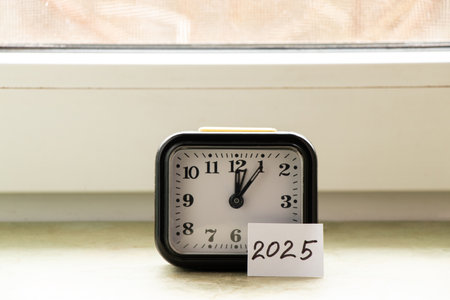 A table alarm clock and a paper card with the text 2025 stand on the window of a house