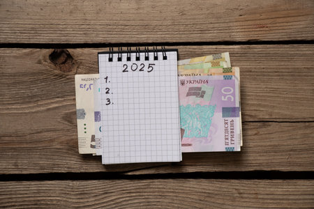 2025 and 123 are written in a notebook and Ukrainian hryvnia, which lies on a wooden table, plans...