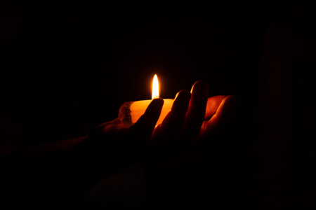 Burning candle in a man's hand in the darkness of the house, candle flame, lighting the houseの写真素材