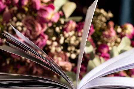 Open book on wooden table at home with dry roses bouquet in roomの写真素材