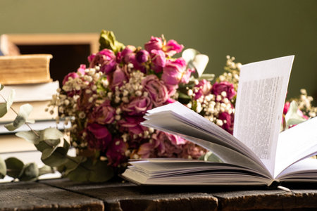 Open book on wooden table at home with dry roses bouquet in room