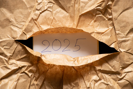The year 2025 is written on white paper and the text is visible from a cut hole in the brown crumpled paper, the year is torn outの写真素材