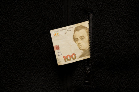 One hundred Ukrainian hryvnia sticking out of the pocket of a black sweater close-up, business and financeの写真素材