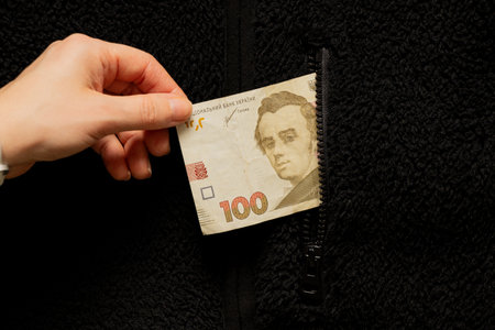 A woman's hand takes out one hundred Ukrainian hryvnias from the pocket of a black sweater, business...