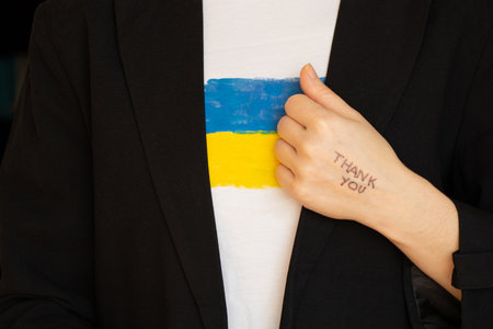 Thank you is written on the hand of a girl who is dressed in a black business jacket and a T-shirt with the flag of Ukraine, words of gratitudeの写真素材
