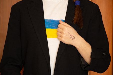 Thank you is written on the hand of a girl who is dressed in a black business jacket and a T-shirt with the flag of Ukraine, words of gratitudeの写真素材