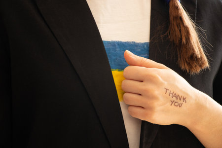 Thank you is written on the hand of a girl who is dressed in a black business jacket and a T-shirt with the flag of Ukraine, words of gratitudeの写真素材