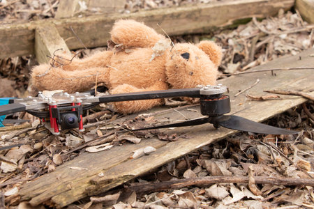 A downed FPV drone lies in the ruins of a destroyed abandoned house next to a child's brown teddy bearの写真素材
