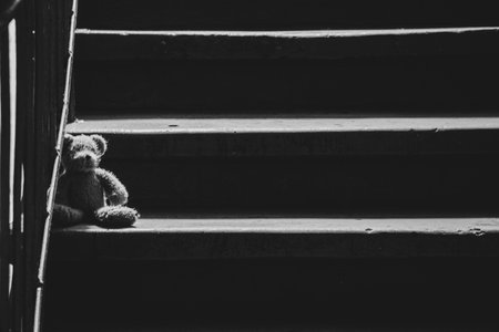 A child's teddy bear sits in the entrance of an old house during the war, an abandoned toy, black and white photoの写真素材