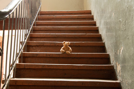 A brown child's teddy bear sits in the entrance of an old house in Ukraine during the war, an abandoned toy, helplessnessの写真素材