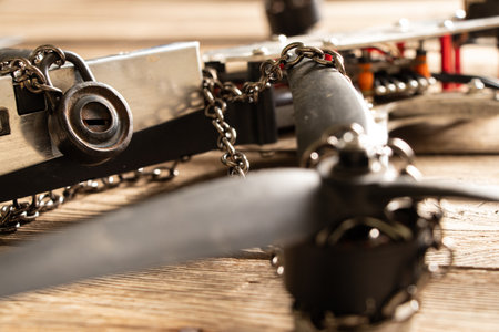 A downed FPV drone lies on a wooden board wrapped in a chain with a rusty padlockの写真素材