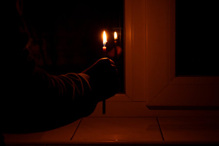 A girl's hand holds a candle near a window in an apartment without light, people without lightの写真素材