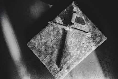 A wooden homemade cross made of branches tied with a rope lies on a book on a leather background, prays, faith in God and religionの写真素材