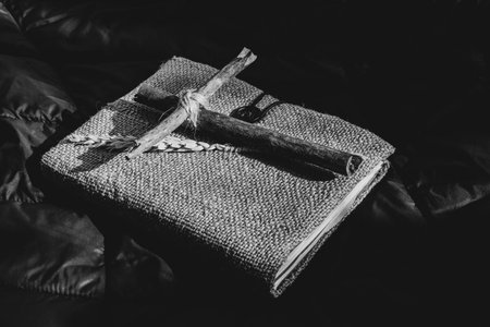 A wooden homemade cross made of branches tied with a rope lies on a book on a black cloth, prays, faith in God and religionの写真素材