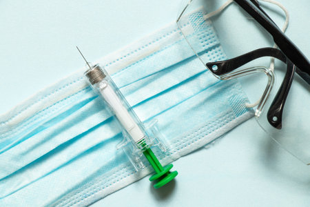 Pre-filled syringe lies on medical mask and glasses on blue background, syringe for injection, medicine and treatmentの写真素材
