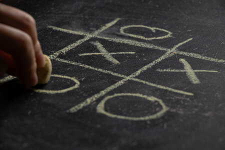 Children's game tic tac toe drawn on a school blackboard and a woman's hand with chalk, play tic tac...