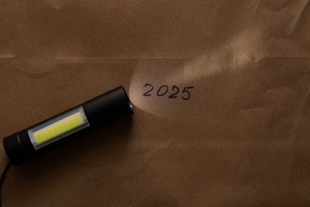 Pocket portable black flashlight with LED bulbs shines on brown paper in darkness,lantern