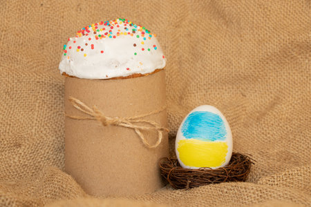 Easter egg with the image of the flag of Ukraine in the nest and Easter cake on the background of...