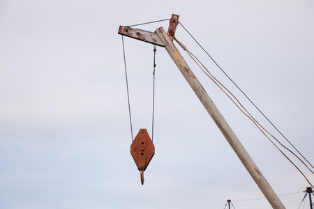Old crane with metal hook against blue sky in the daytime outdoorsの写真素材