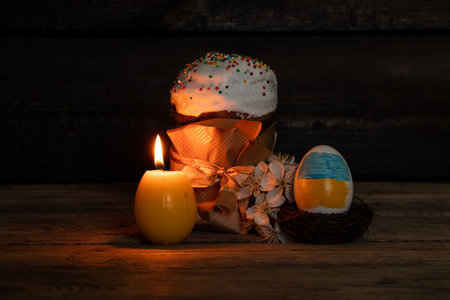 Easter egg with painted flag of Ukraine, kulich and blossoming branch of cherry and candle in the...