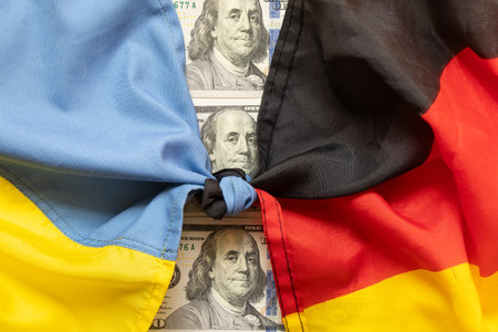 Flags of Germany and Ukraine tied in a knot against a background of dollars, symbolizing union, finance and politicsの写真素材