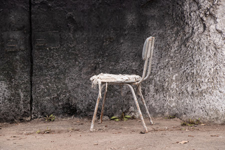 Old dirty torn chair stands near concrete black wall as a place to rest, rest on breakの写真素材