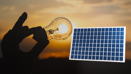 Hand holding a light bulb against a sunset background next to a 3D model of a solar panel, transition to sustainable energy, energy efficiencyの写真素材