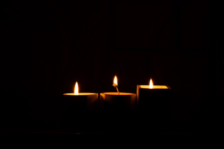 Three homemade candles in plaster candlesticks burn in the dark of the house, candle flame, candles in the darkの写真素材