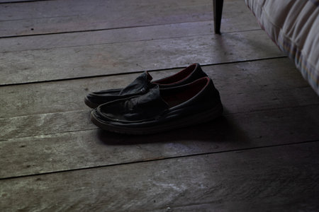 Old men's slippers stand on a wooden floor near a bed in a house without renovation, shoes near the bedの写真素材