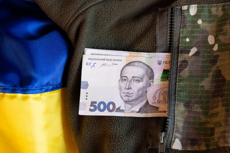 Five hundred hryvnias lie in a pocket in a military uniform on the flag of Ukraine, salary and...
