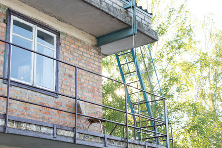 Facade of a brick building with a fire escape and a chair on a balcony in the summer in the sun in Ukraineの写真素材