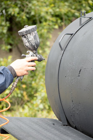 Painting a metal barrel with a spray gun outdoors in Ukraineの写真素材