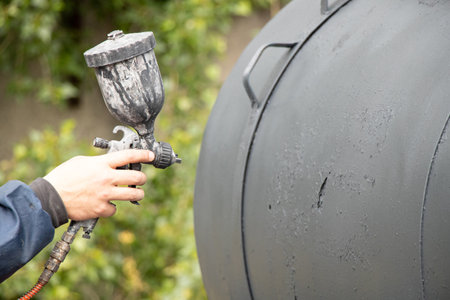 Painting a metal barrel with a spray gun outdoors in Ukraineの写真素材