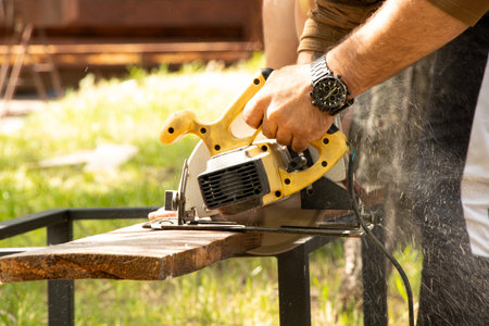 A man saws a board with a circular saw on a table outside and sawdust spills, sawing a board