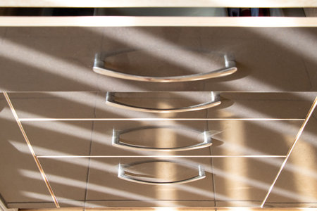 Kitchen brown pull-out drawers with handles in an apartment on the kitchen with a striped shadow from the curtains on the windowの写真素材