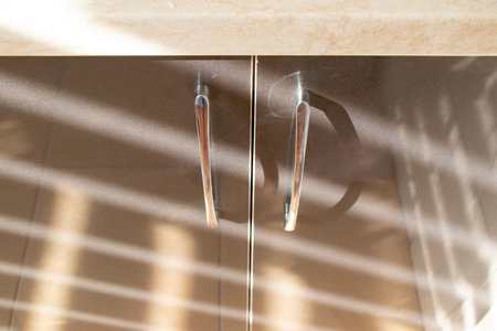 Kitchen brown drawers with handles in the apartment on the kitchen with a striped shadow from the curtains on the windowの写真素材