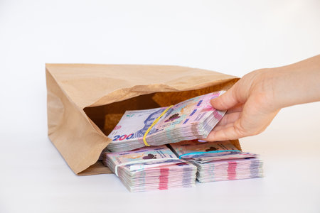 A woman's hand takes out packs of Ukrainian hryvnias that are lying in a paper bag on a white background, money and profit, 200 hryvnias in packsの写真素材