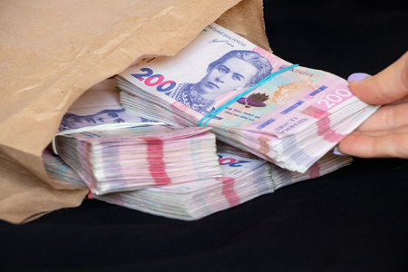 A woman's hand takes out packs of Ukrainian hryvnias that are lying in a paper bag on a black background, money and profit, 200 hryvnias in packsの写真素材
