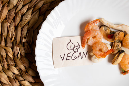 Shrimps and squids lie in a plate with a note vegan on a straw background, lunchの写真素材