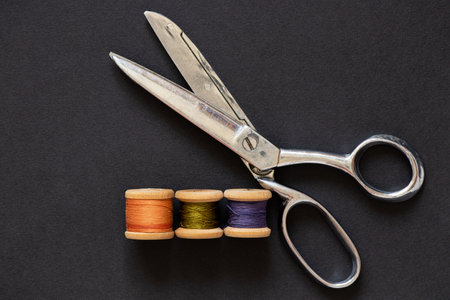 Dressmaker scissors and wooden spools of thread on black background, sewing and cutting toolsの写真素材