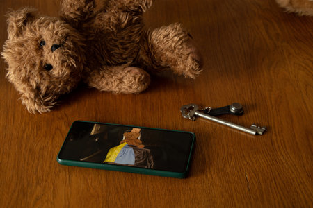 Teddy bear, old key and smartphone with photo of girl with suitcase, farewell and leaving home because of warの写真素材