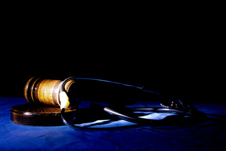 Judge's gavel and stethoscope on blue cloth in the dark with backlight, medical trial in court, law and justiceの写真素材