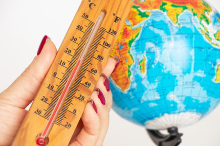 Thermometer in a woman's hand against the background of a globe, climate change and global warmingの写真素材