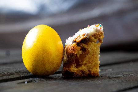 Golden Easter egg and a piece of Easter cake with icing and sprinkles on a wooden table at home, Easter holidayの写真素材